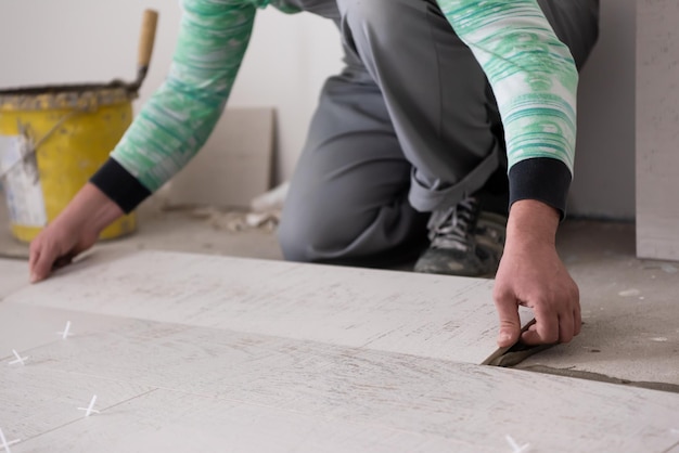 Квалифицированный рабочий укладывает керамическую плитку с эффектом дерева на пол Рабочий укладывает ламинат на строительной площадке новой квартиры
