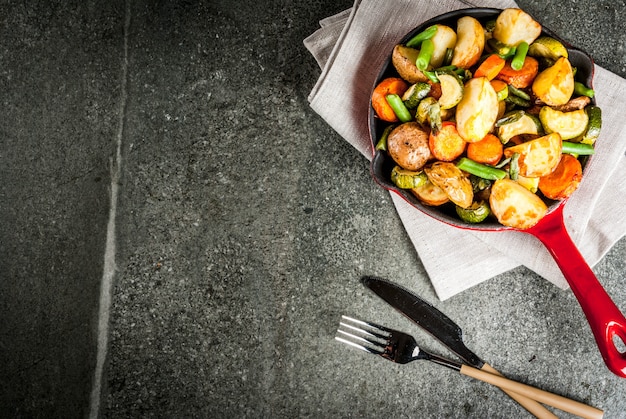 Skillet with  fried seasonal autumn vegetables (zucchini, potatoes, carrots, beans), on black stone table  top view