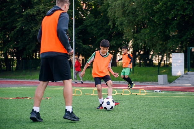 スポーツフィールドで彼のコーチと一緒に運動しているサッカーユニフォームの熟練したプレーヤー