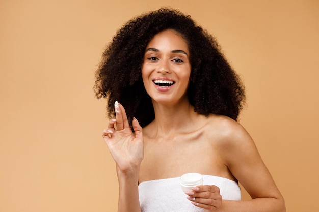 Skin care concept pretty african american lady applying moisturizing face cream posing and smiling