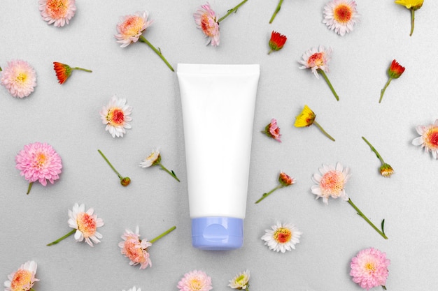 Skin care cosmetics tube on floral background top view