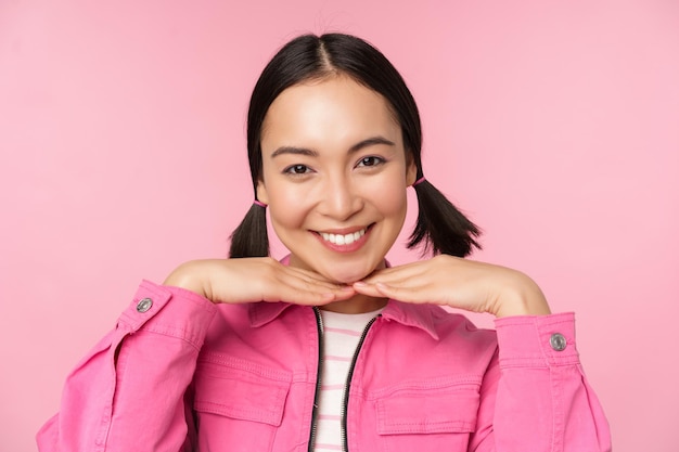 피부 관리 및 미용 개념 아름다운 아시아 소녀는 분홍색 배경에 대해 포즈를 취한 깨끗하고 건강한 얼굴 피부를 보여주며 웃고 있습니다.