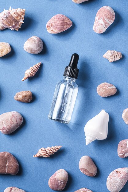 Skin care essence oil dropper in glass bottle near to seashells and pebbles