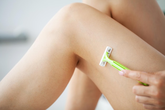 Skin care and health, fit woman shaving her legs with razor.