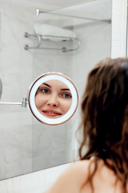 スキンケア 髪を触り鏡を見ながら微笑む女性