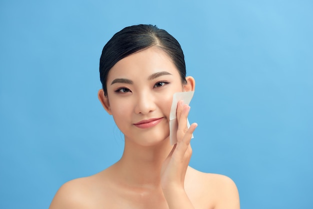 Skin care. Young woman removing oil from face using blotting papers.