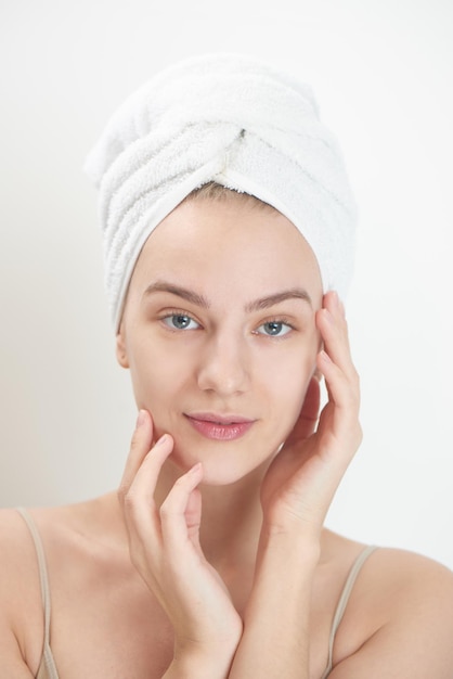 Photo skin care. young woman on white background with towel on head touching her clean skin on the face