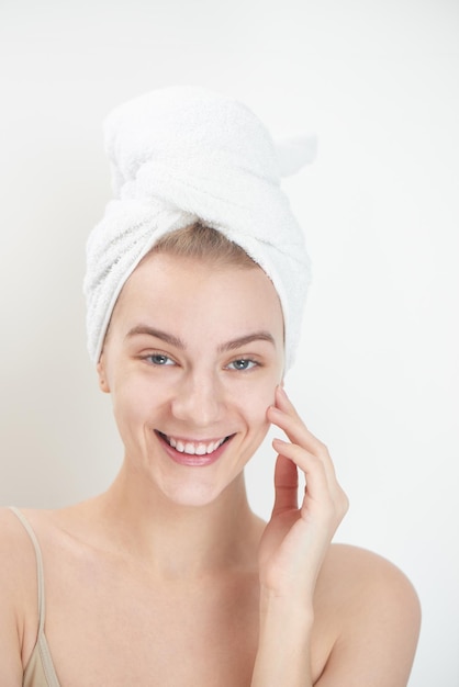 Skin care. Young woman on white background with towel on head touching her clean skin on the face