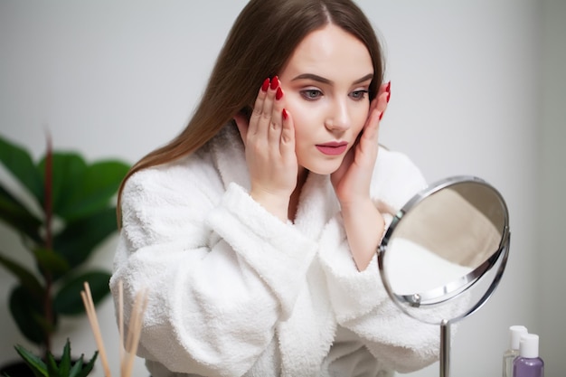 Skin care, young woman with pure face skin examines face in mirror.