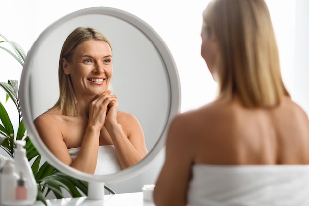 Skin rejuvenation beautiful mature woman looking in mirror at her reflection