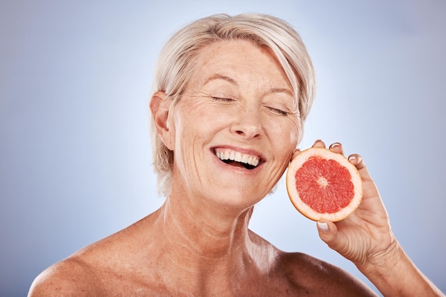 Красота по уходу за кожей и пожилая женщина с грейпфрутом для здоровья и красоты лица на фоне серого макета студии Возбужденная счастливая и пожилая модель с улыбкой для фруктовой диеты