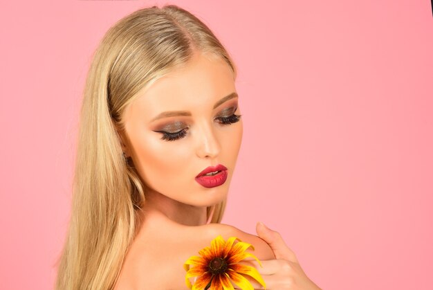 Skincare, beauty, skin health concept - gorgeous blonde girl with perfect makeup, flower on shoulder. Attractive sexy blonde woman with long hair bright makeup holds flower. Copy space for advertise.