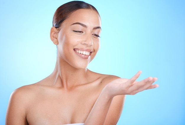 Skincare beauty woman and hand with mockup space for natural cosmetics product by blue background Happy model skin glow and aesthetic with makeup for cosmetic mock up in studio with excited smile