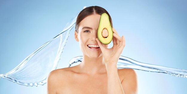 Skincare beauty and woman portrait with avocado for natural skin dermatology cosmetic product Water splash and face of aesthetic model in studio for sustainable self care for health and wellness