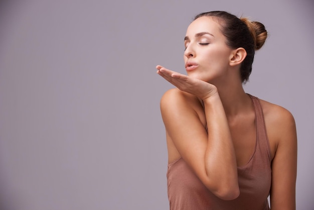 Skincare blow kiss and young woman in studio with health wellness and dermatology routine Cosmetic confident and female person with natural facial treatment and flirt gesture by gray background