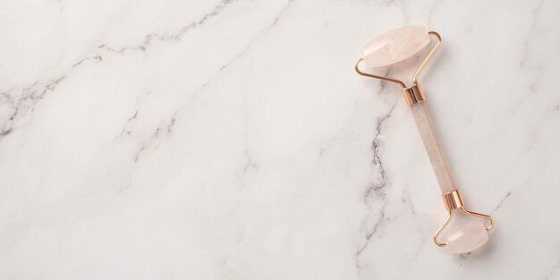 Skincare concept Top view photo of rose quartz roller on white marble background with empty space