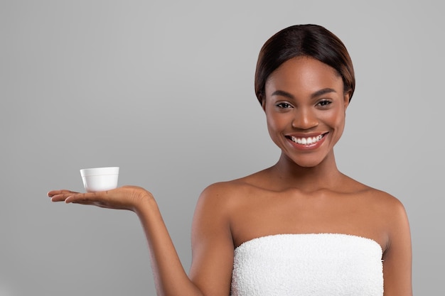 Skincare cosmetic young smiling black woman holding jar with moisturising cream