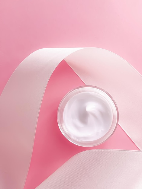 Skincare cosmetics face cream moisturiser jar and white silk ribbon on pink background beauty product flatlay closeup