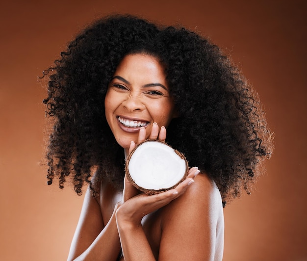 Skincare hair care and black woman marketing coconut for wellness of skin against a brown studio background advertising cosmetics and face portrait of an african model with fruit for beauty