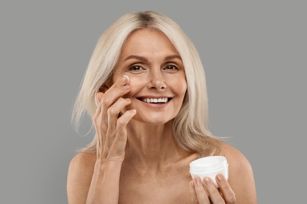 Skincare routine beautiful mature woman applying moisturizing cream on face