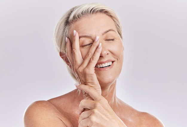 Skincare wellness and beauty with a senior woman touching her smooth skin and beautiful face with her hand in studio on a grey background Natural health and skin care with a female feeling happy