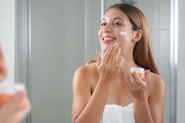 Skincare woman applying cream on her cheek Face moisturizing nourishing invigorating treatments Enjoying relaxing time