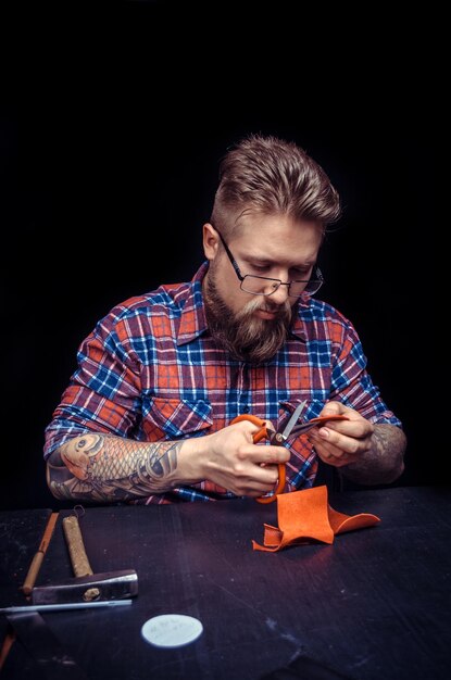 Skinner producing leather workpiece at leather shop./Currier manufacturing new leather product at his shop.