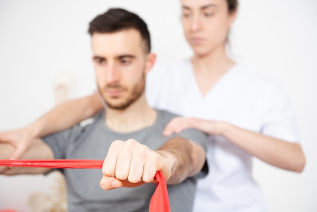 Skinny man making rehabilitation exercises with a pilates rubber band. Closeup detail of the hand holding the band.