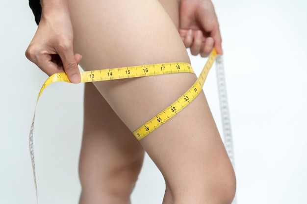 A skinny woman uses a tape measure around her thigh with gray background. Health care concept.