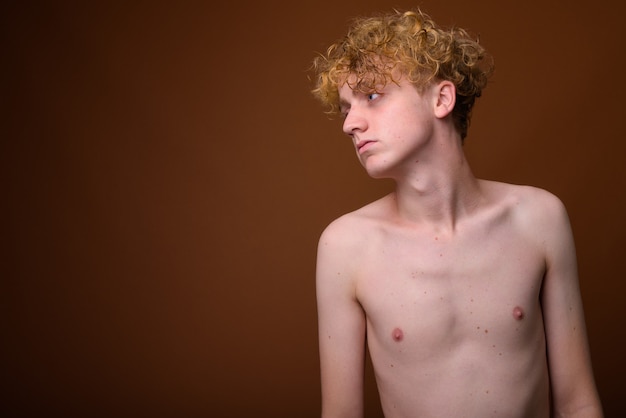Skinny young man with curly hair shirtless on brown
