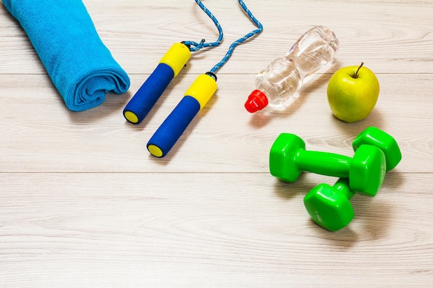 Skipping rope and dumbbells for fitness a towel a bottle of water and an apple in a room or a gym
