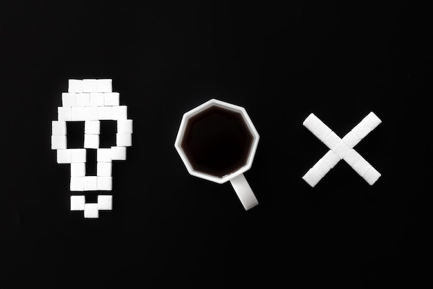 Skull bones from sugar and cup of coffee on black background\
flat lay