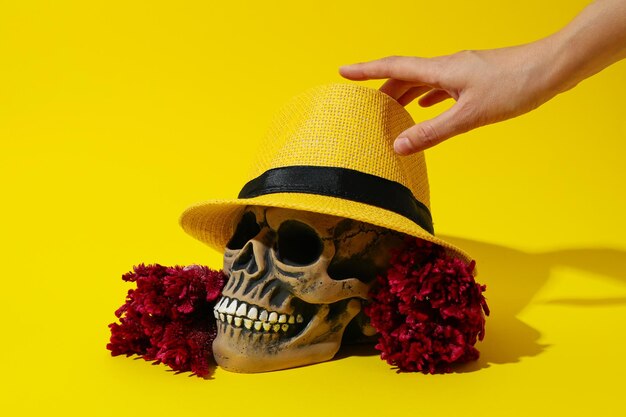 Foto teschio in fiori di cappello e mano femminile su sfondo giallo