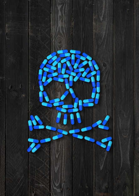 Skull made of blue capsule pills isolated on black wood background. 3D illustration