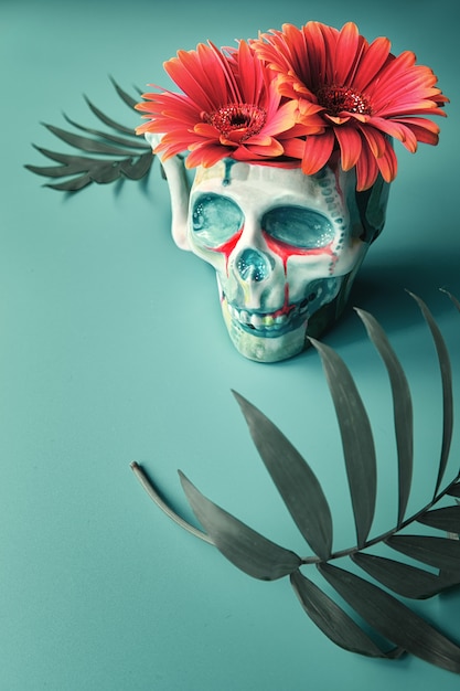 Skull with coral color gerbera flowers and palm leaves