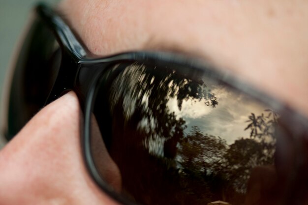 Sky and forest reflected in lenses of black sunglasses