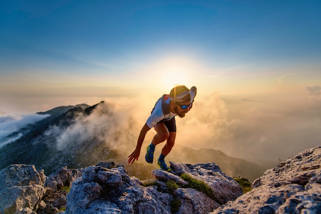 Sky runner man bergop op rotsen bij zonsondergang