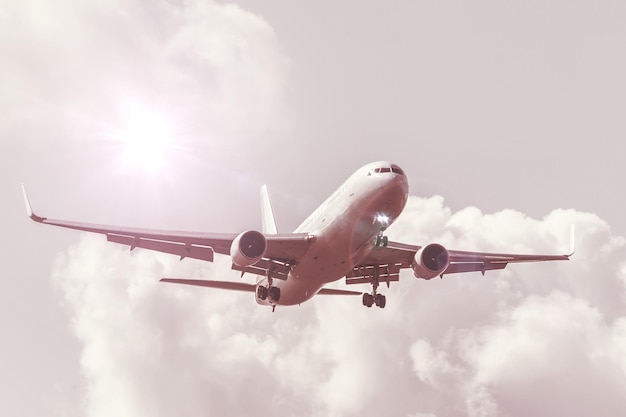 Небо с облаками и солнцем с теплым оттенком, отраженным бликами, большим пассажирским самолетом, приземляющимся в аэропорту