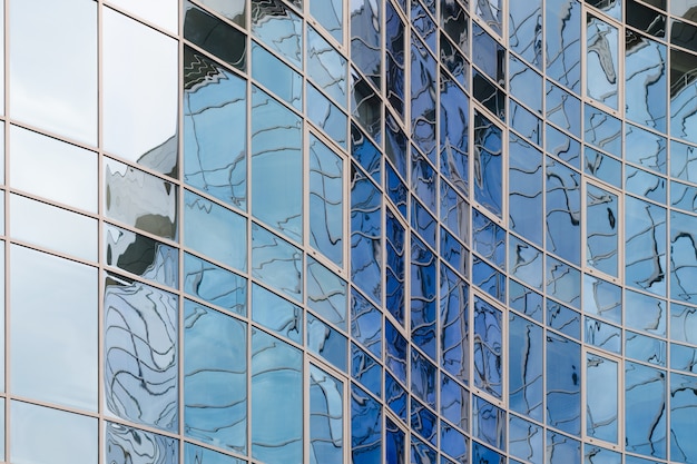 Skyscraper mirror glass surface reflecting cloudy sky, curvy surface