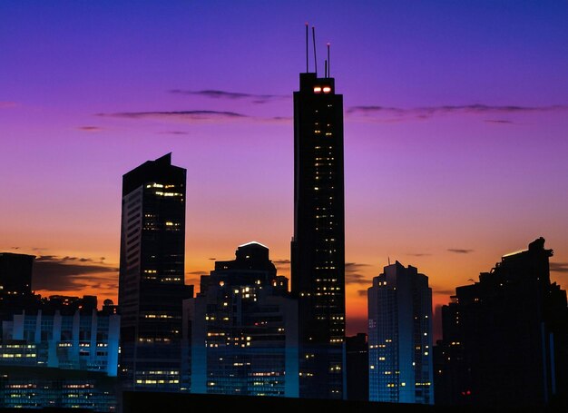Skyscraper silhouette against vibrant city lights at dusk generative ai