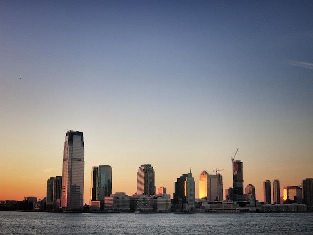 skyscrapers by river against sky during sunset