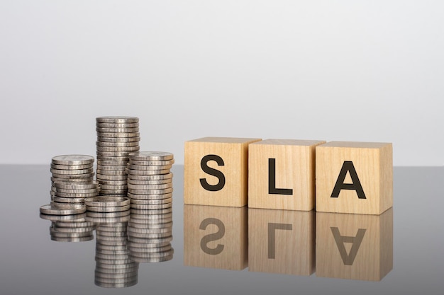 SLA wooden cubes blocks lie on a black background stacks with coins inscription on the cubes is reflected from the surface of the table selective focus SLA short for Service Level Agreement