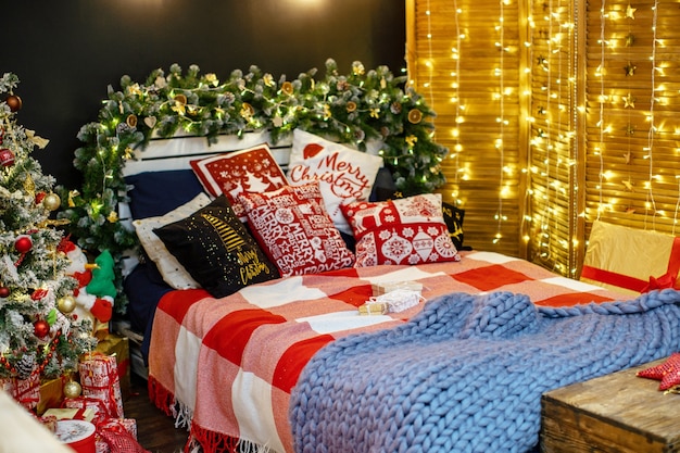 Slaapkamer interieur in donkere decoratie ingericht voor Kerstmis. het bed met donkerblauw linnen en veel kussens is bedekt met een wollen deken van Hypergroot schaapgaren