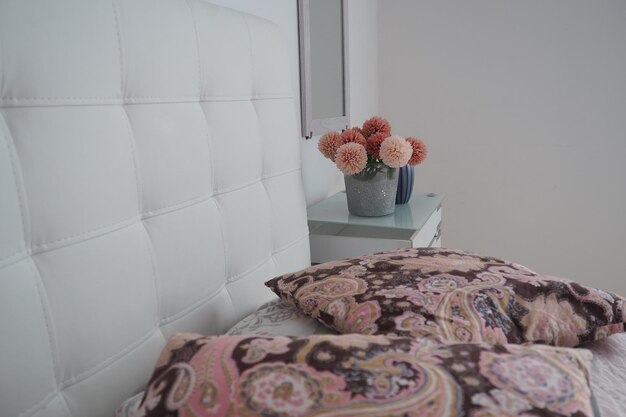Slaapkamer interieur Spiegel aan de muur Een boeket van mooie roze bloemen op een witte tafel in de slaapkamer Interieur Design Bed met wit gestoffeerd hoofdeinde Decoratief kussen