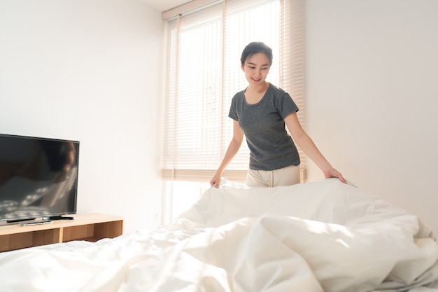 Slaapkamerconcept een vrouwelijke volwassene die de routine doet door de rand van de deken te grijpen om het bed op te maken na het opstaan in de ochtend.