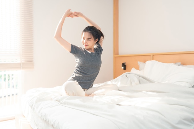 Slaapkamerconcept in de ochtend het mooie meisje dat net wakker wordt en haar lichaam strekt op het bruine houten bed.