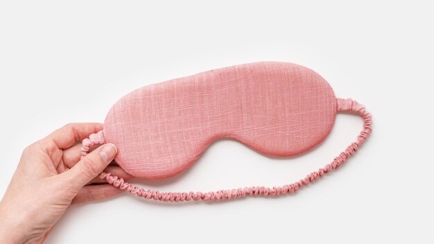 Foto slaapmasker voor een gezonde slaapkwaliteit in de hand van een vrouw op een witte achtergrond van roze kleur