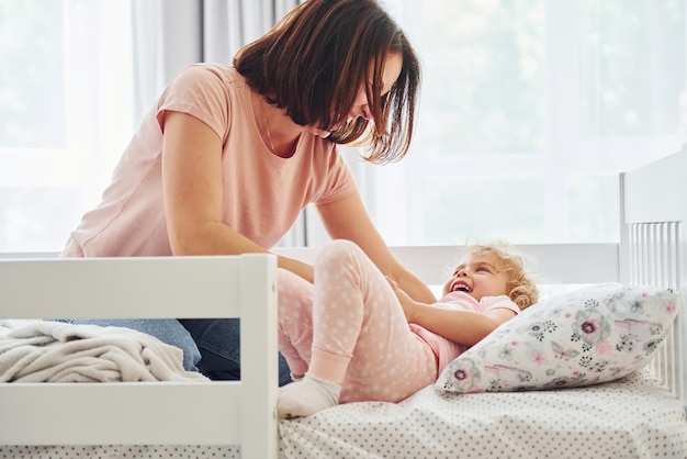 Slaaptijd Jonge moeder met haar dochtertje in vrijetijdskleding samen binnenshuis thuis