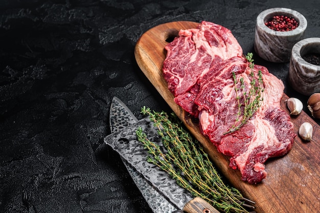 Slager gemarmerd vlees Steaks op houten snijplank rauw rundvlees ribeye steaks Zwarte achtergrond Bovenaanzicht Kopieer ruimte