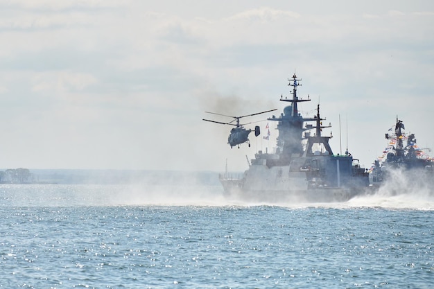 Slagschepen oorlogsschepen korvet tijdens marine-oefeningen en helikopter manoeuvreren over water in de Oostzee. Oorlogsschepen, helikopters en boten voeren taken uit op zee, militaire oorlogsschepen zeilen, Russische marine